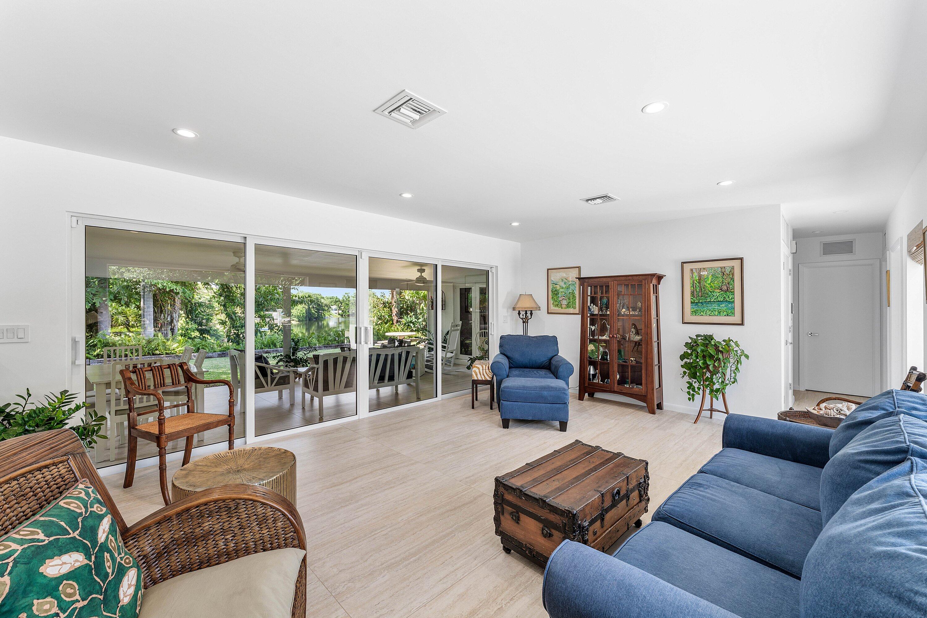 Living room with blue sofas and wicker chairs beside sliding glass doors overlooking water.