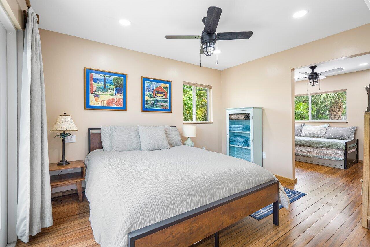 Bedroom with a large white bed, wood floors, ceiling fan, and adjoining sleeping nook.