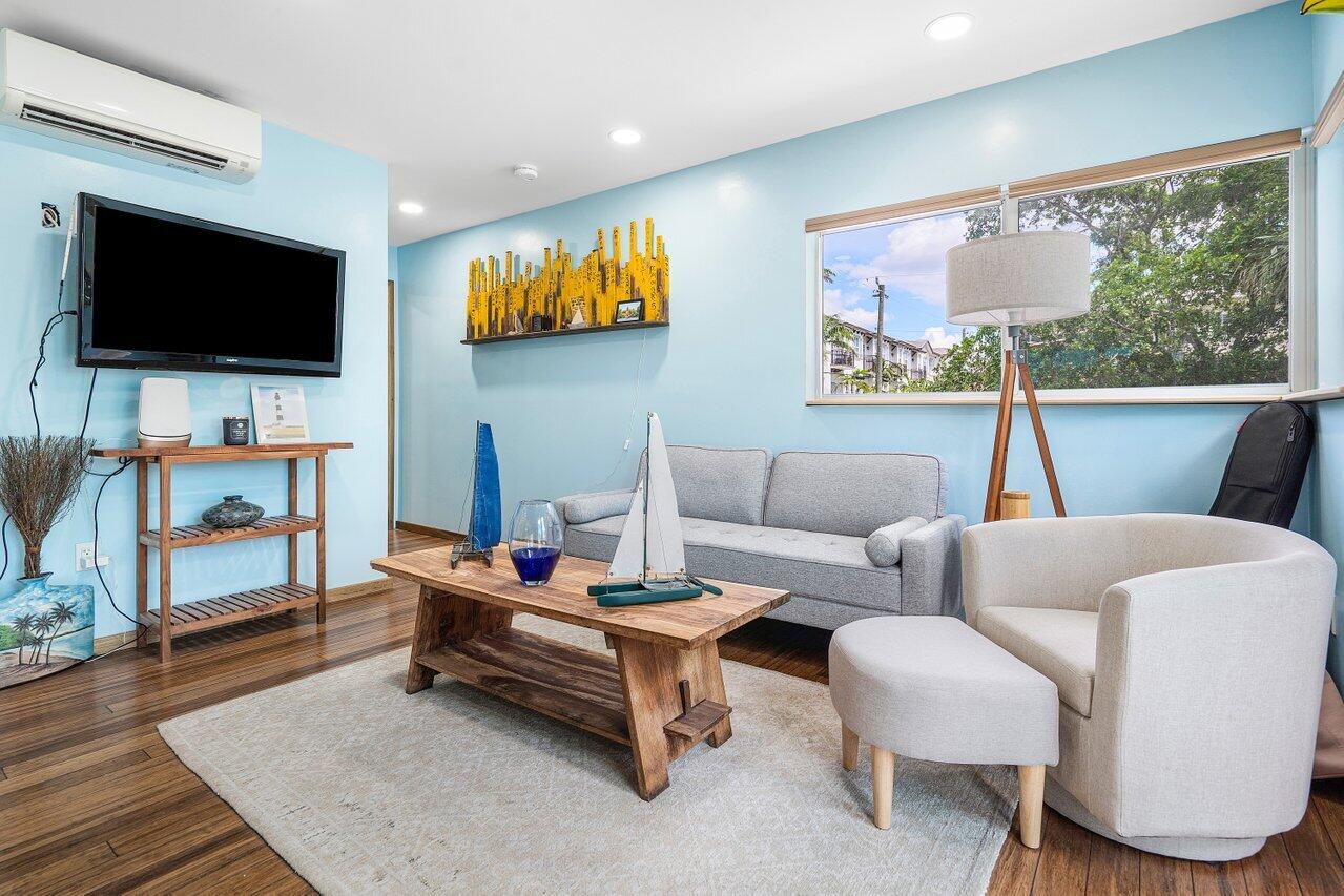 Living room with pale blue walls, gray seating, wood floors, and a large window.