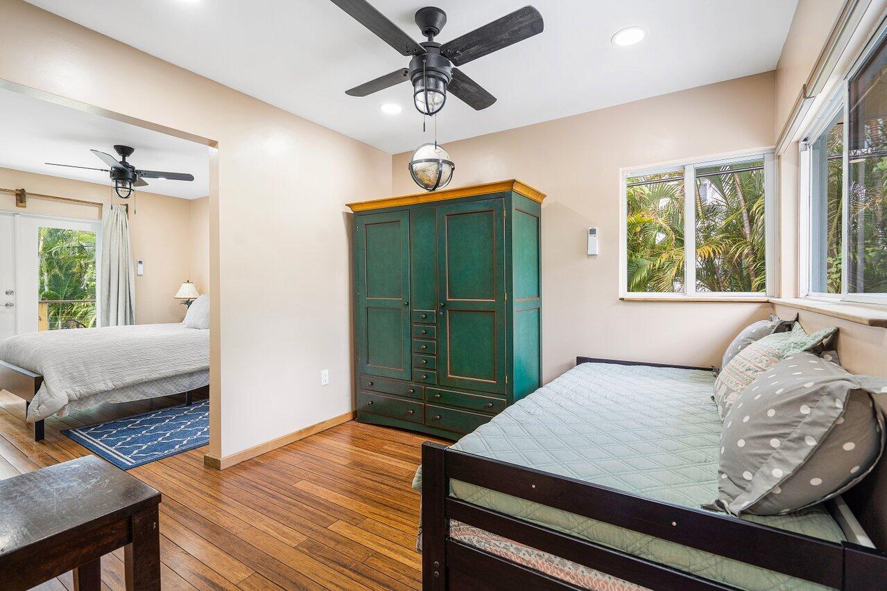 Furnished bedroom with a teal armoire, dark wood bed, and windows facing tropical foliage.