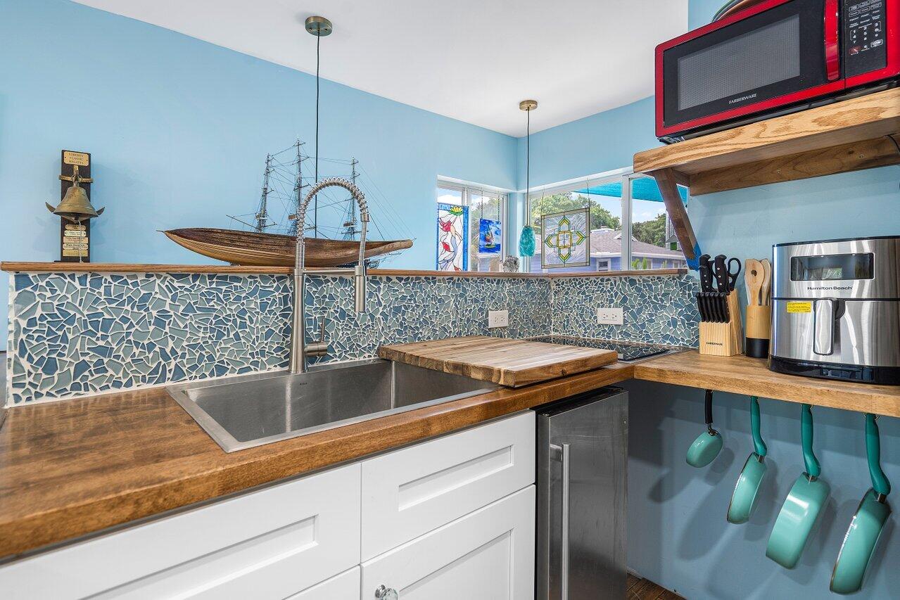 Kitchen with mosaic tile backsplash, wood counters, stainless sink, and turquoise hanging cookware.