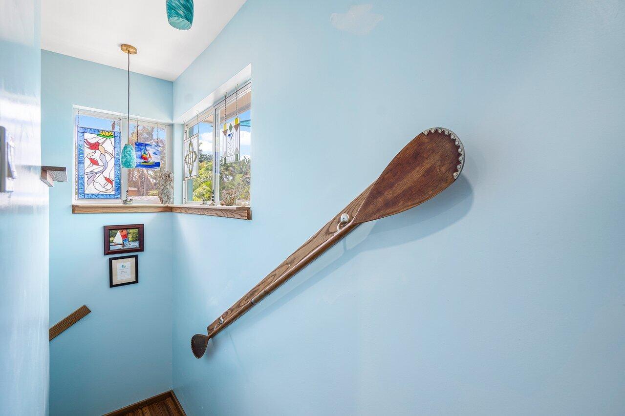 Blue-walled staircase with a mounted wooden paddle and stained-glass panels beside sunny corner windows.