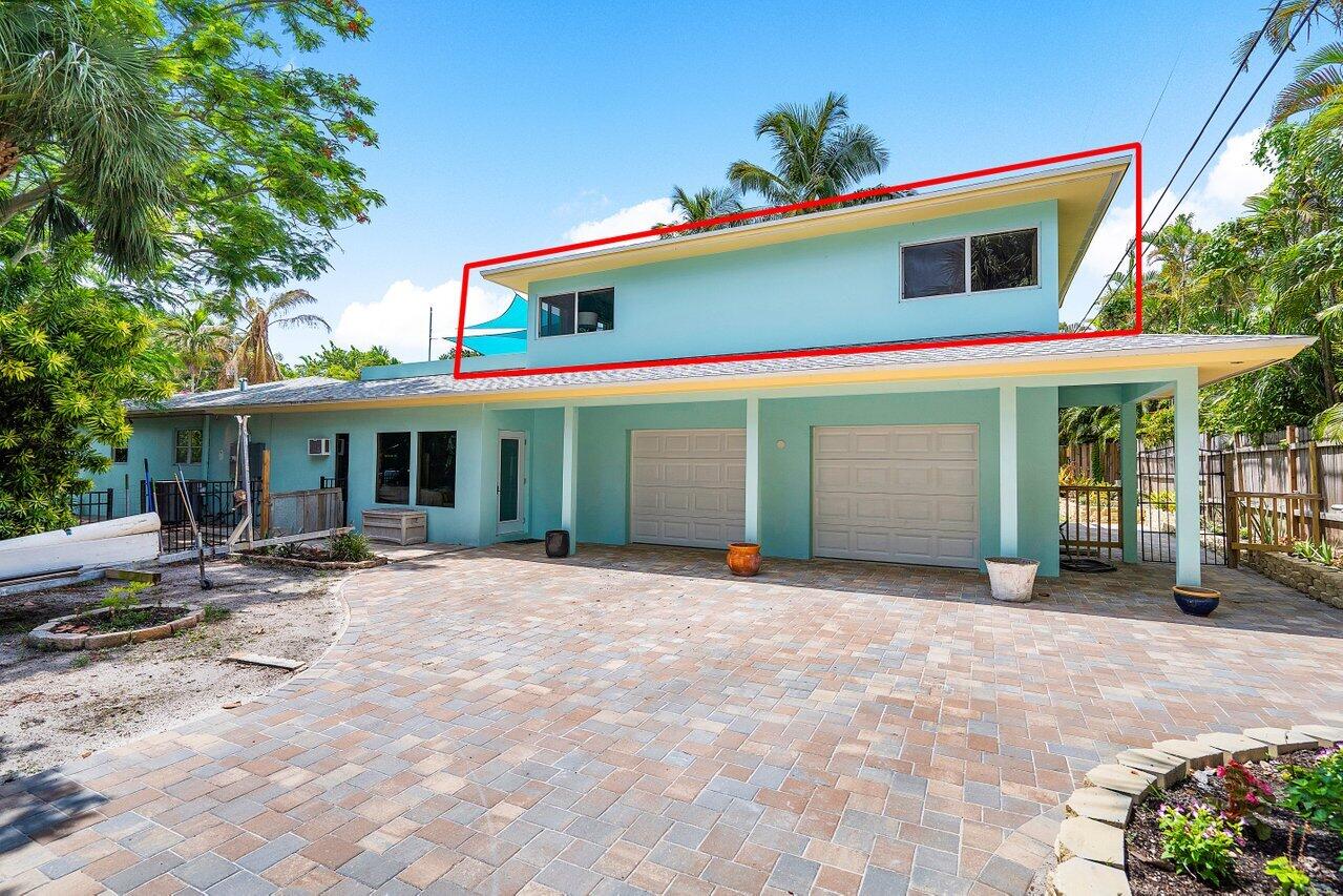 Turquoise two-story home with a red outline around its upper level and a wide paver driveway.