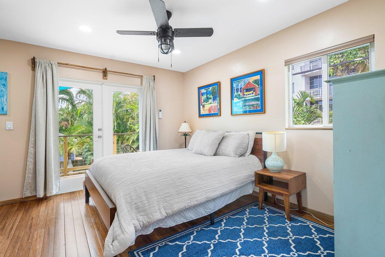 Bedroom with a large bed, blue patterned rug, and glass doors opening onto greenery.