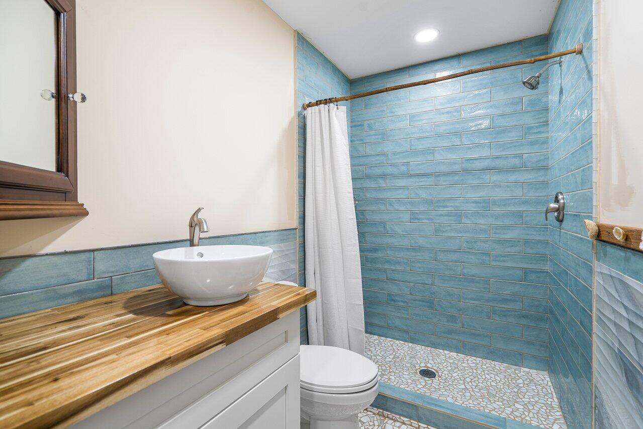 Bathroom with a blue-tiled shower, mosaic floor, and vessel sink on a wood countertop.