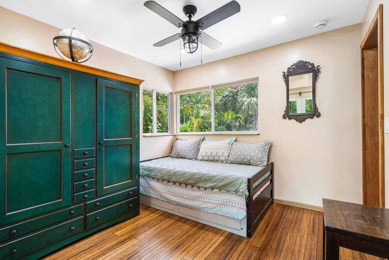 Bedroom with a dark teal built-in wardrobe and daybed beneath windows overlooking tropical greenery.