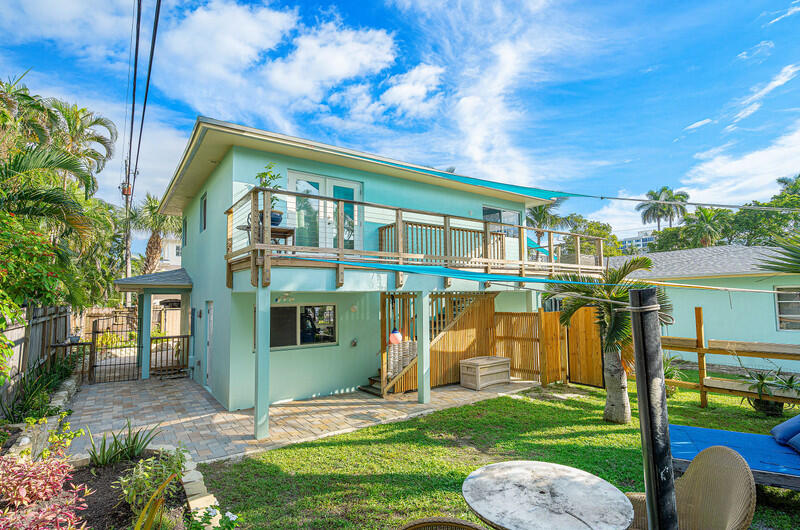 Two-story aqua house with a wooden balcony overlooking a fenced backyard and partial pool.