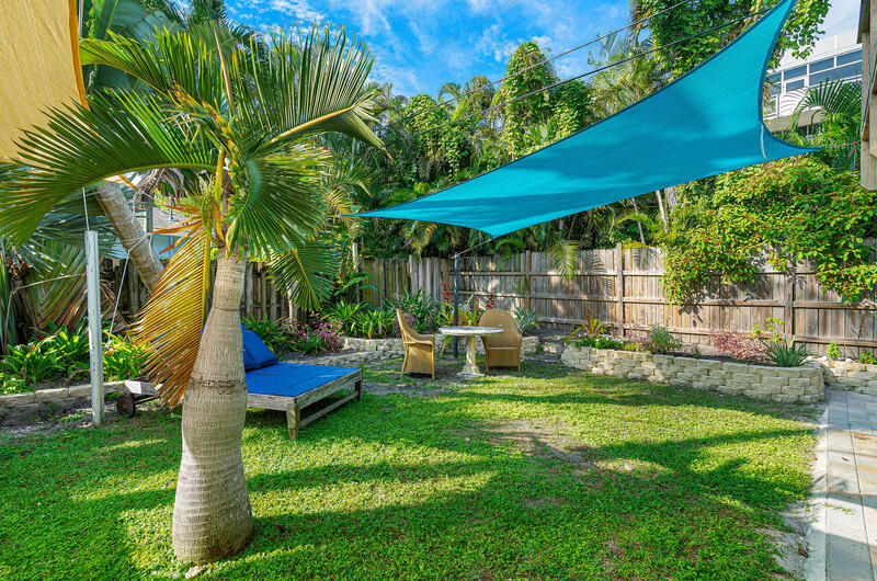 Backyard with a turquoise shade sail over a lawn, palm trees, and outdoor seating.