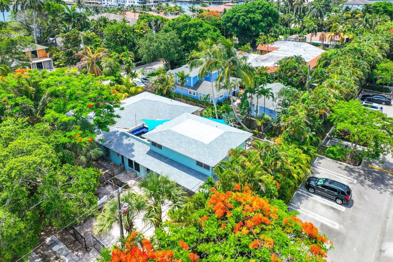 Turquoise house surrounded by palms and tropical landscaping, viewed from above beside a street.