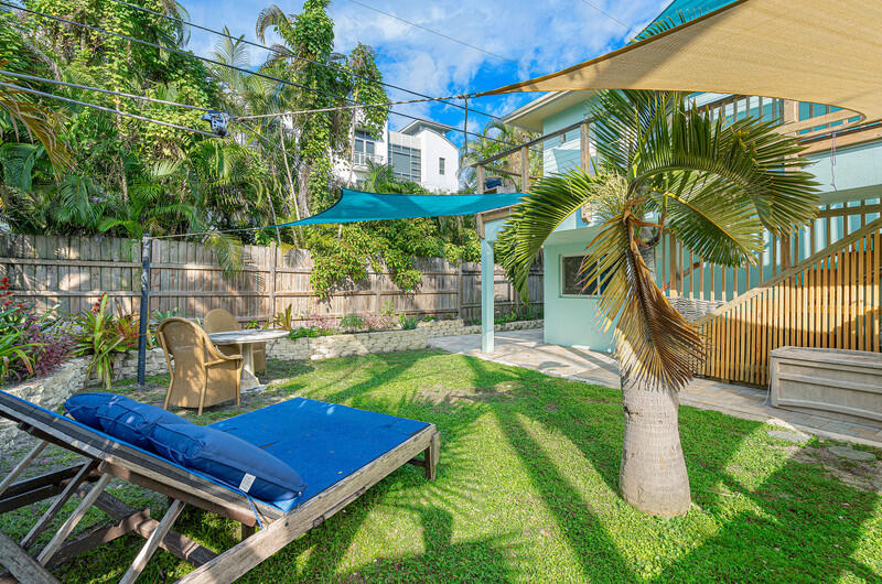 Backyard with a palm tree, lawn, patio seating, blue lounge cushions, and shade sails.