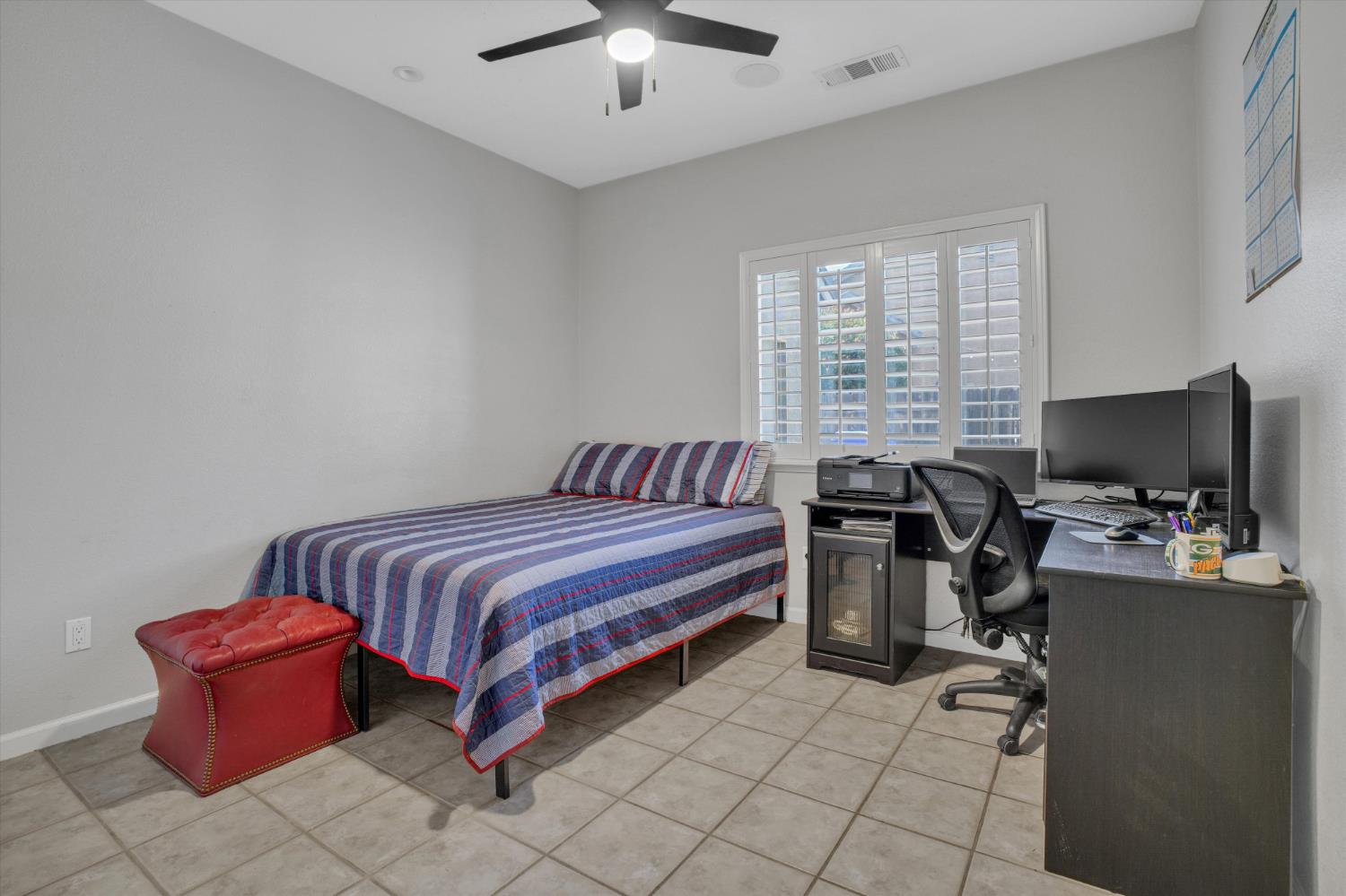Bedroom with a striped bedspread and a computer desk beside a shuttered window.