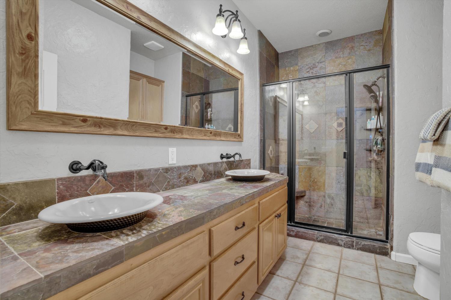 Bathroom with a double vessel-sink vanity and a glass shower tiled in varied earth tones.