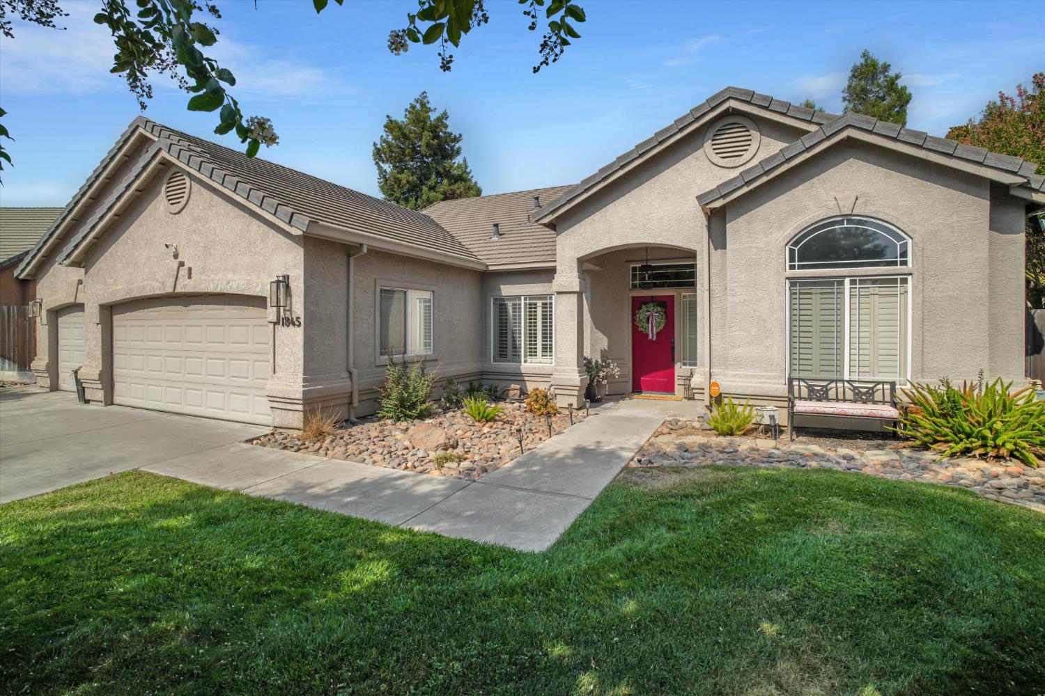Single-story stucco home with a two-car garage, red front door, and arched window.