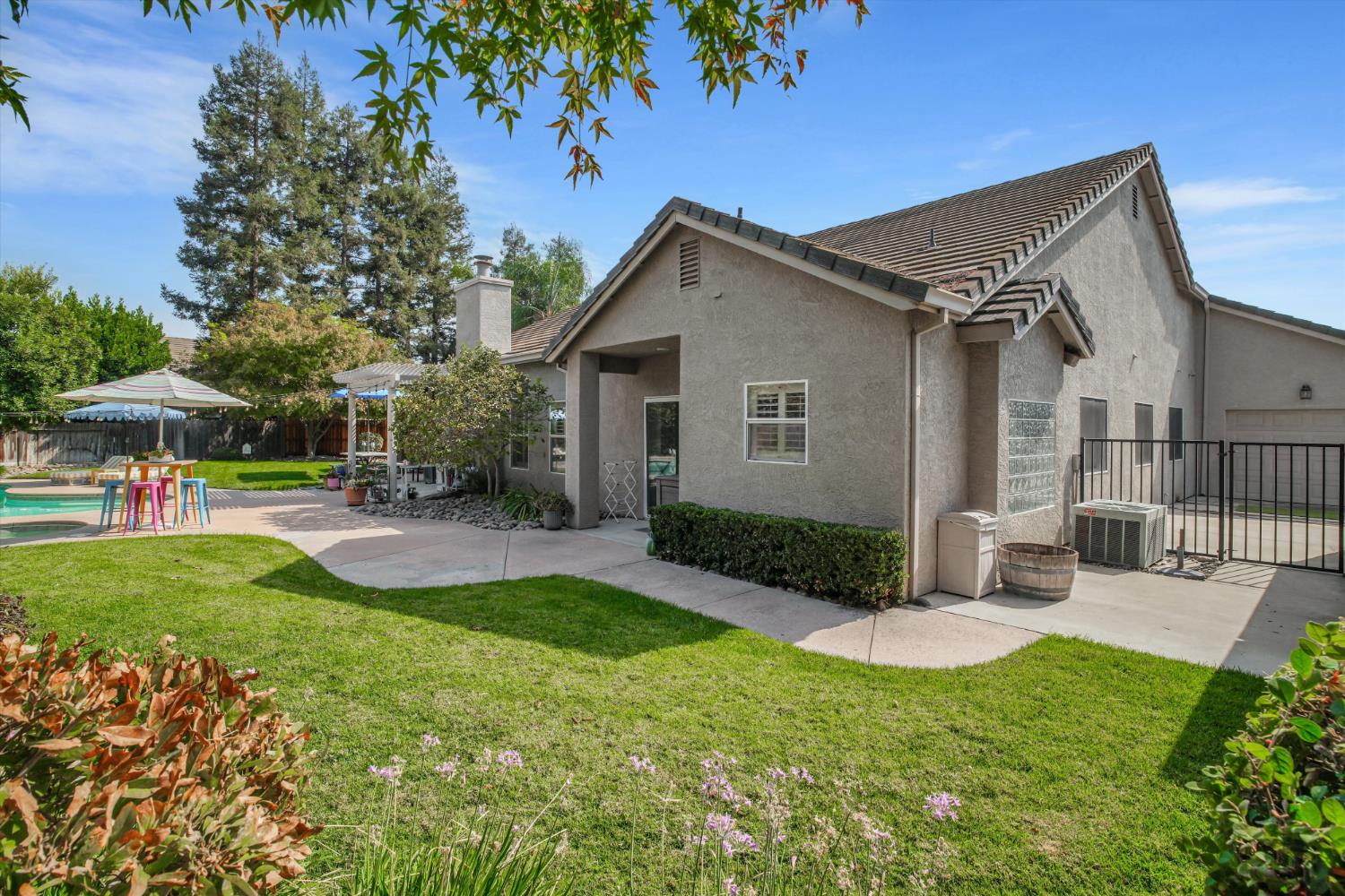 Home’s rear exterior with a swimming pool, landscaped lawn, and patio seating.