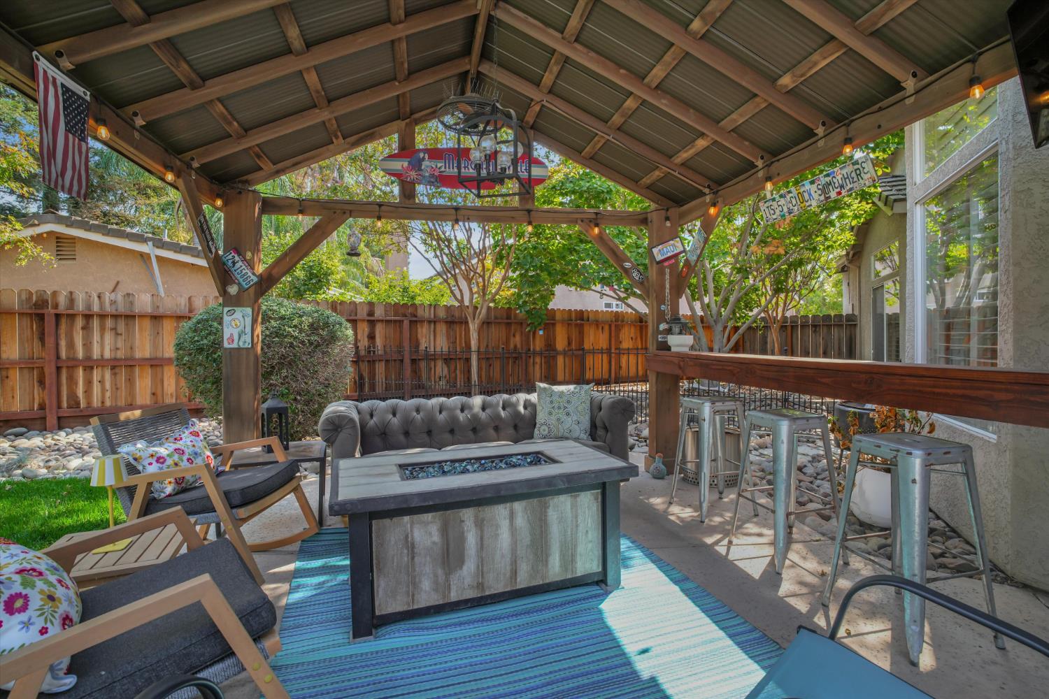 Covered backyard patio with a timber pergola, lounge seating, and a rectangular fire table.