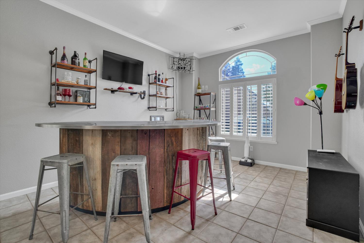 Bar area with a curved rustic wood counter, metal stools, bottle shelves, and arched window.