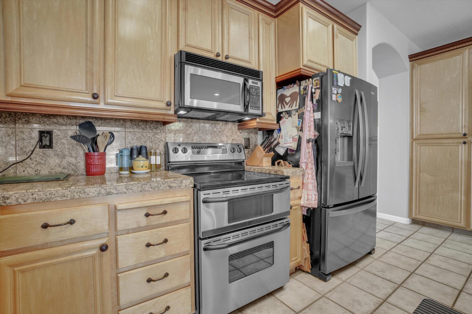 Kitchen with light wood cabinetry, granite counters, stainless steel appliances, and tile flooring.