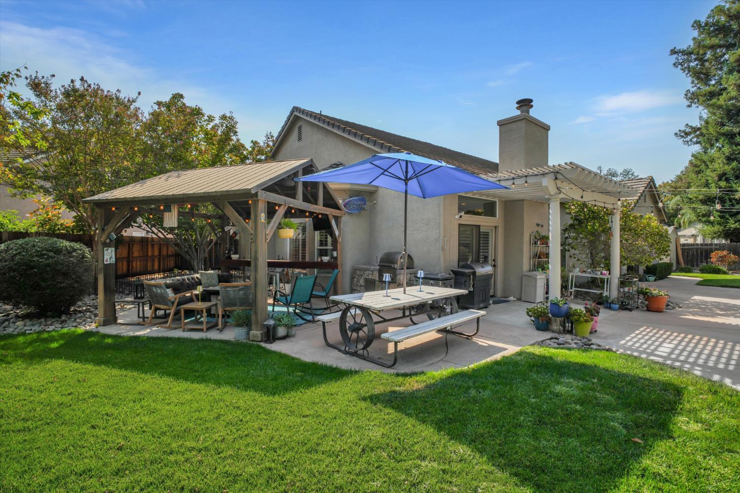 Home backyard patio with covered seating, blue umbrella, outdoor dining table, and grills.