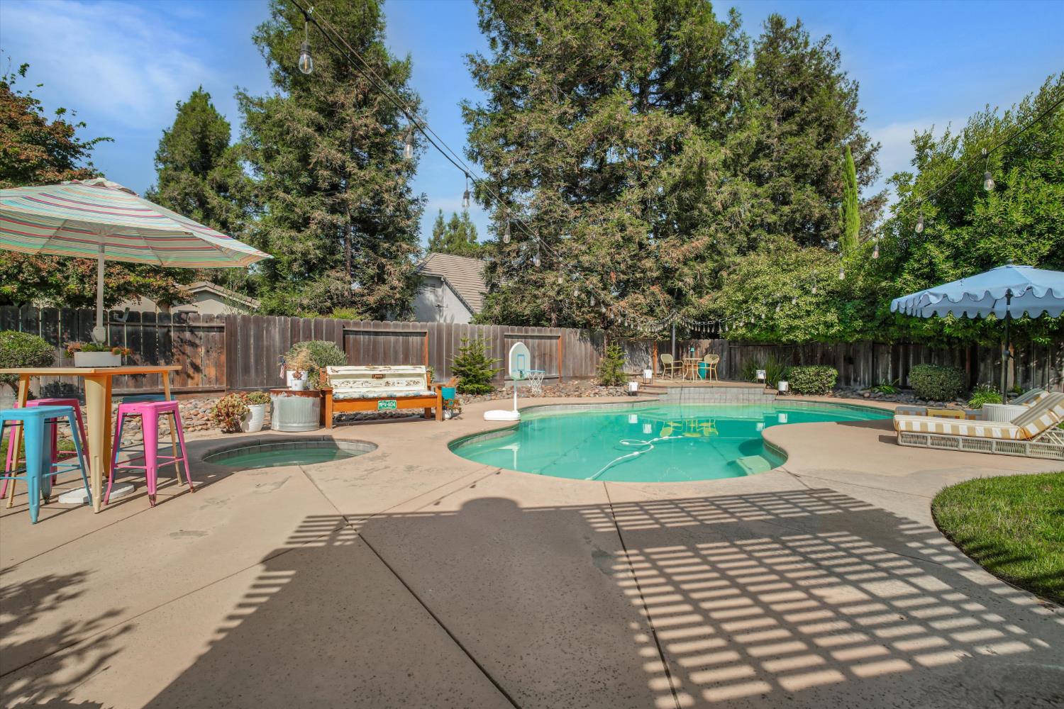 Backyard pool and attached spa surrounded by a shaded patio, lounge chairs, and mature trees.