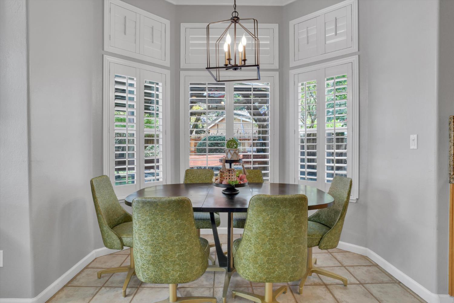 Dining nook with a round table, green chairs, and tall shuttered windows.