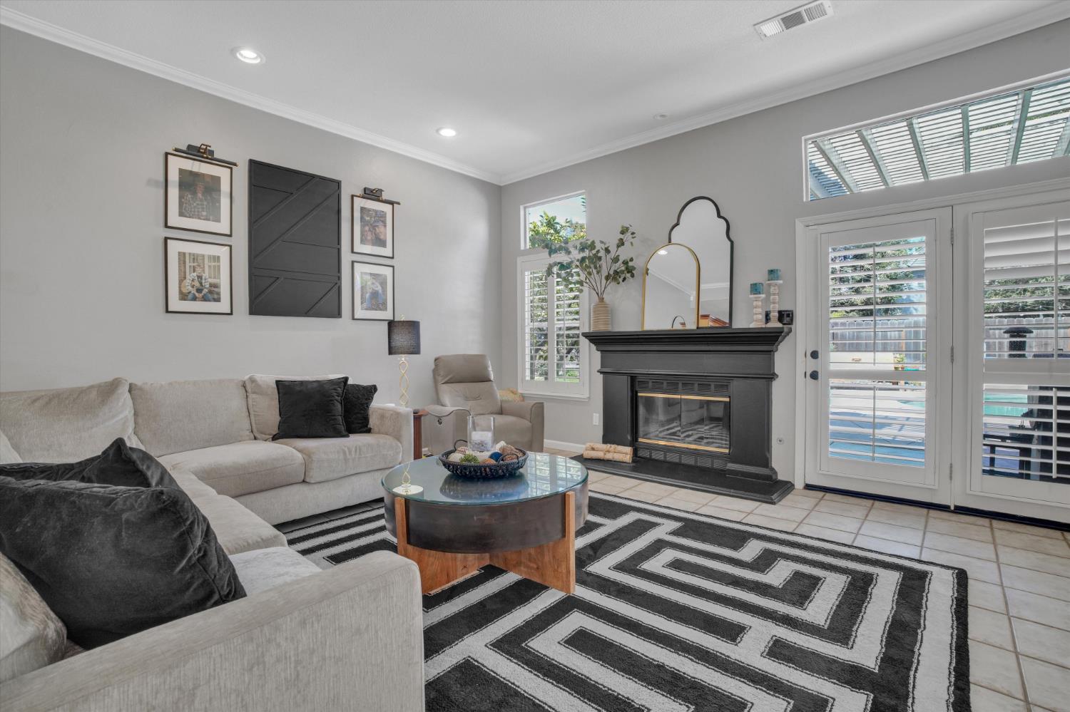 Living room with a black fireplace, geometric rug, and shuttered patio doors overlooking a pool.