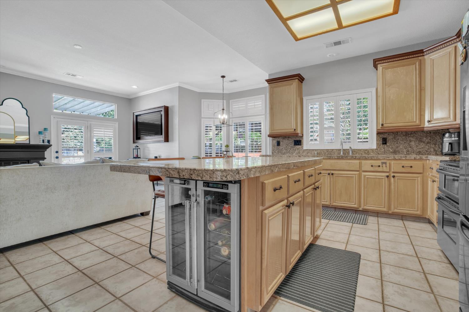 Kitchen with a granite island, light wood cabinets, and a glass-door wine refrigerator.