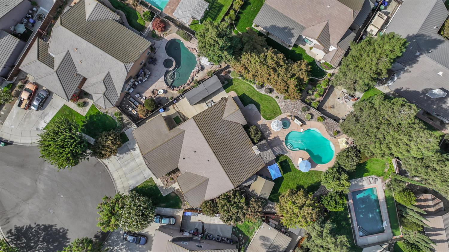 Aerial view of a tree-lined cul-de-sac with homes, landscaped yards, and several swimming pools.