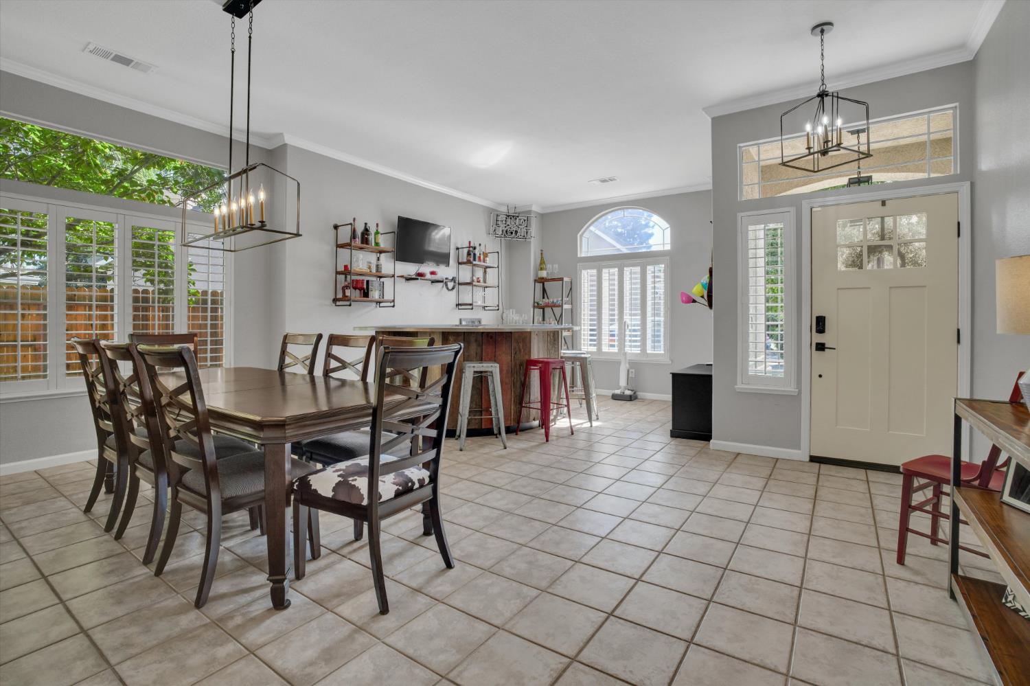Dining room with a dark wood table, tiled floor, shuttered windows, and a kitchen island with bar stools.