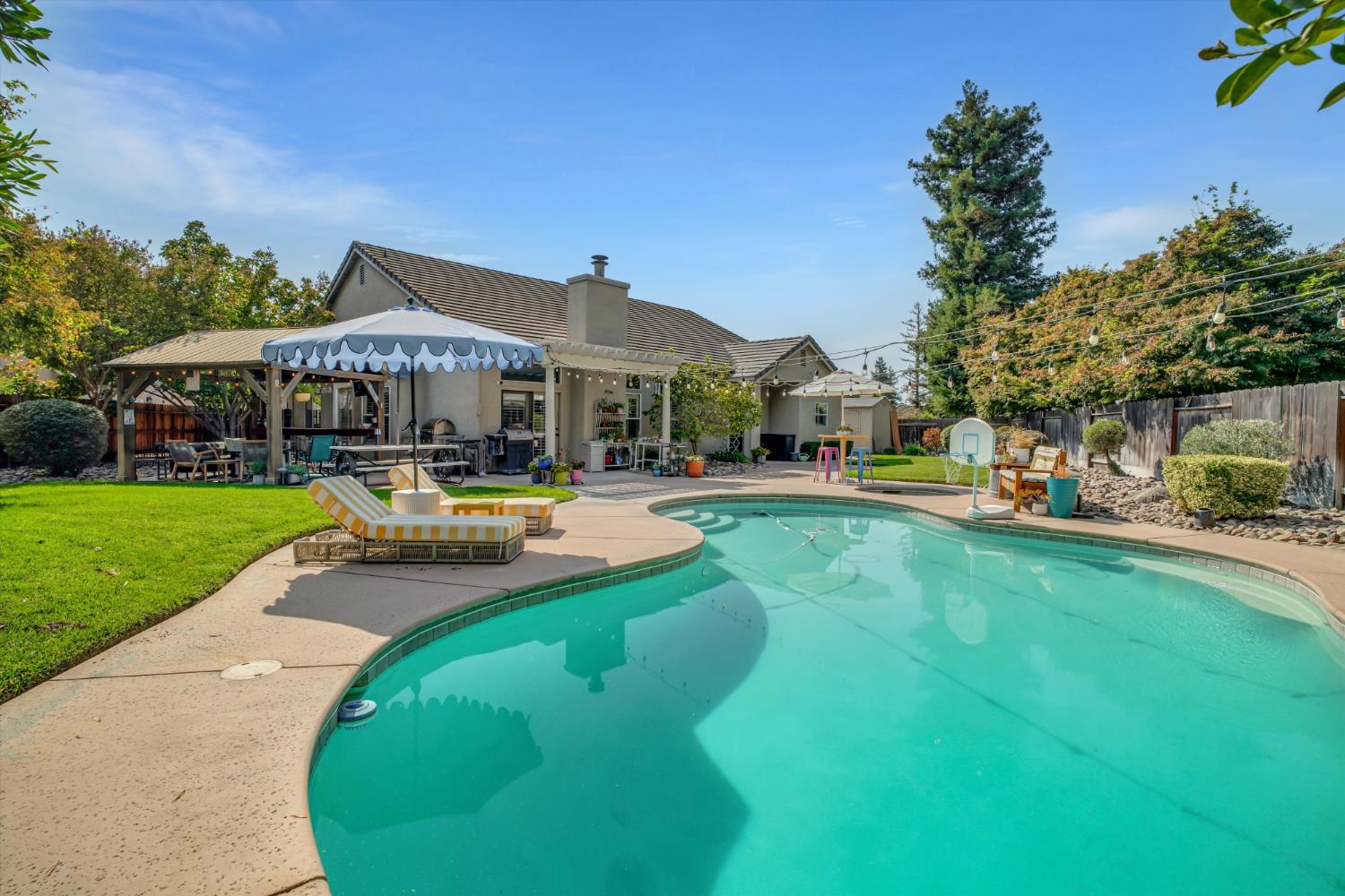 Backyard pool with curved turquoise water, patio seating, and a covered pergola.