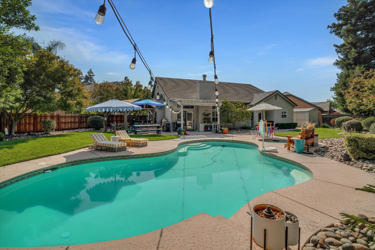 Backyard swimming pool with patio seating, shade canopies, and string lights.