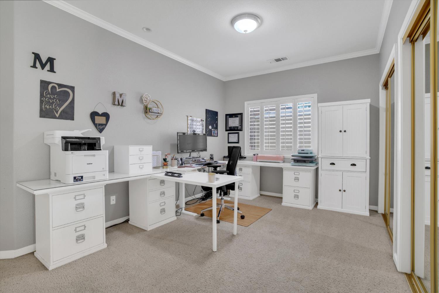 Home office with white desks and cabinets, a computer, printer, and plantation shutters.
