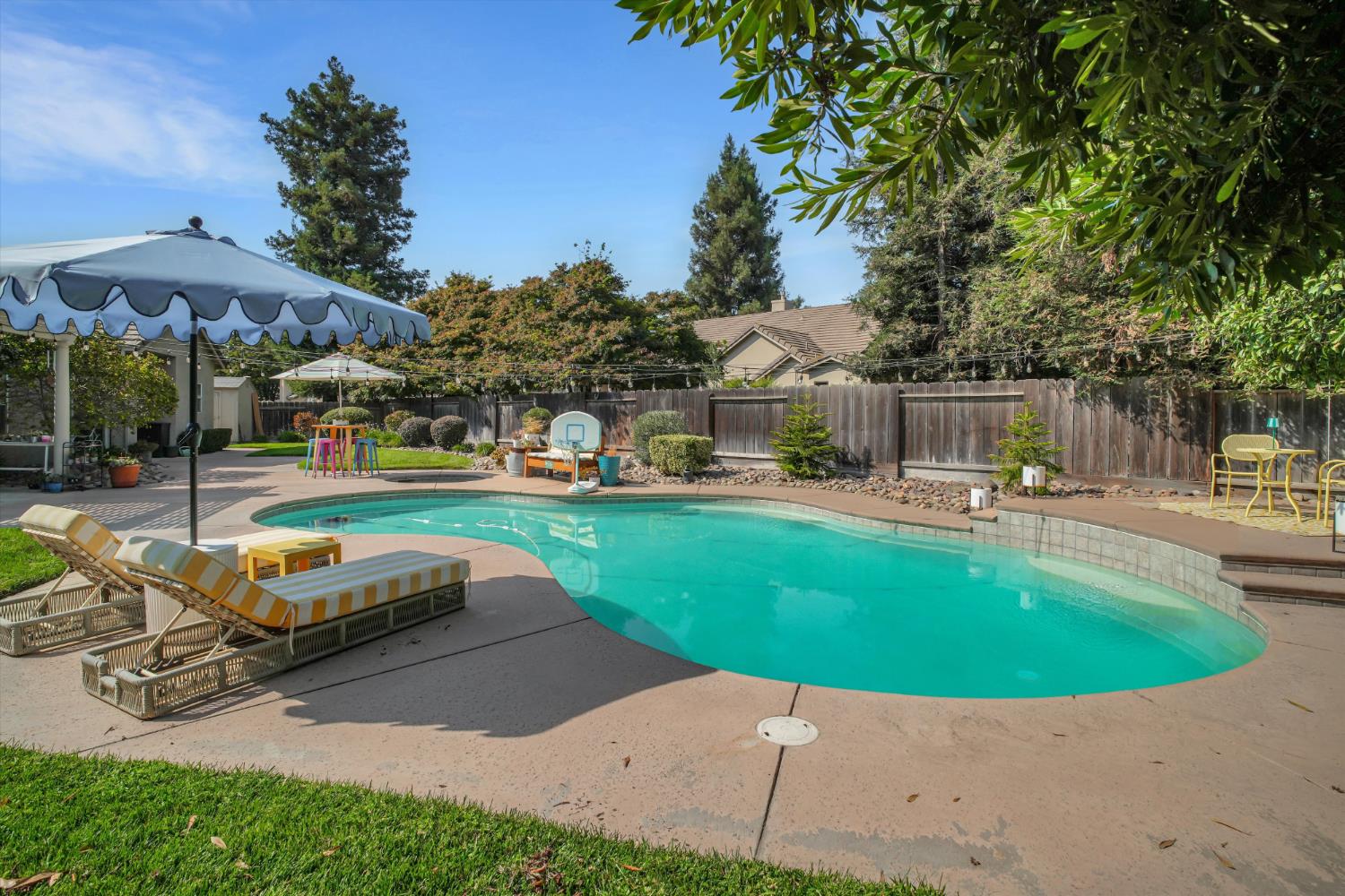 Backyard swimming pool with striped lounge chairs, patio umbrellas, and a basketball hoop.