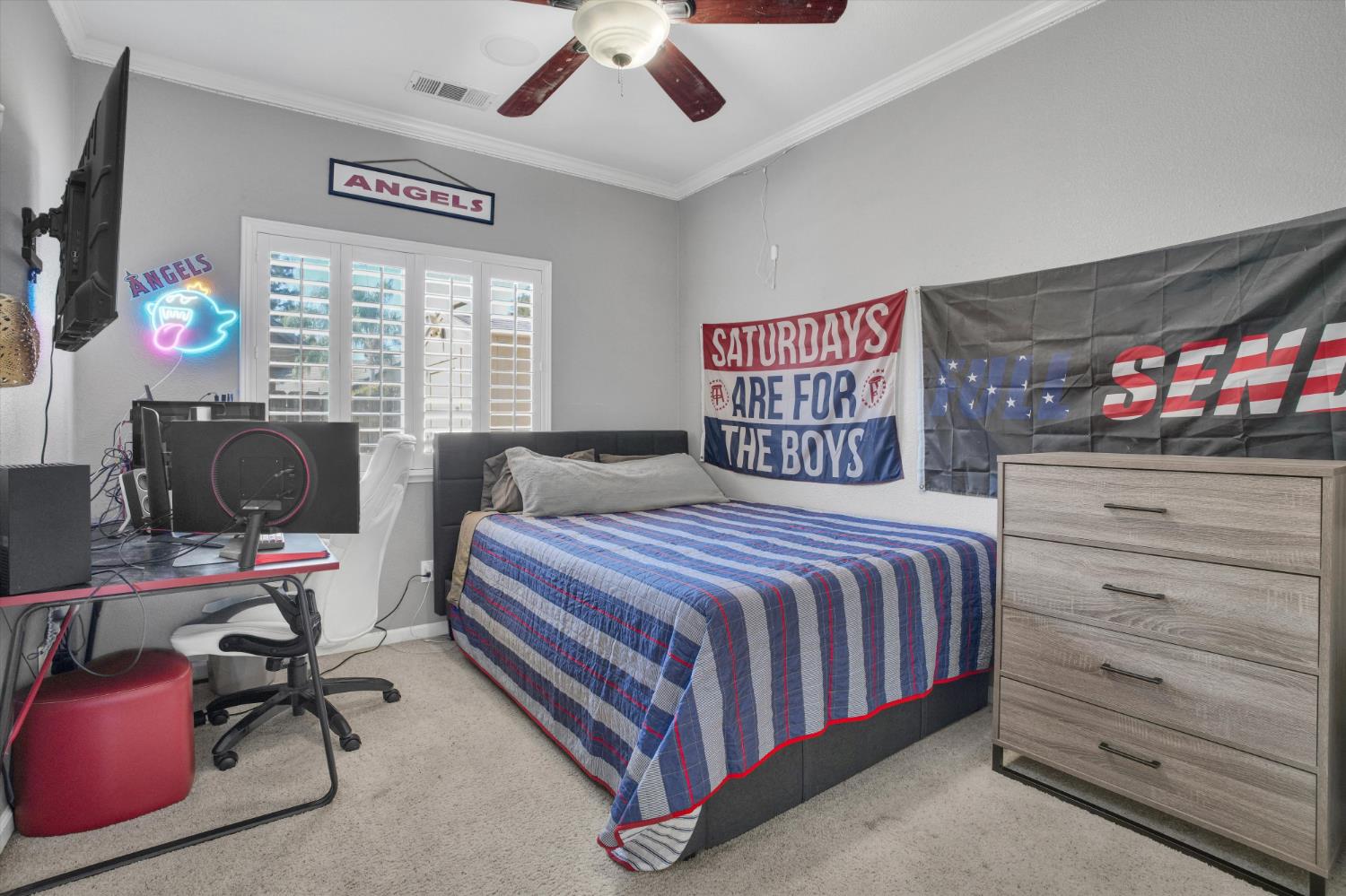 Bedroom with a striped bedspread, gaming desk, dresser, and Angels sports decorations.