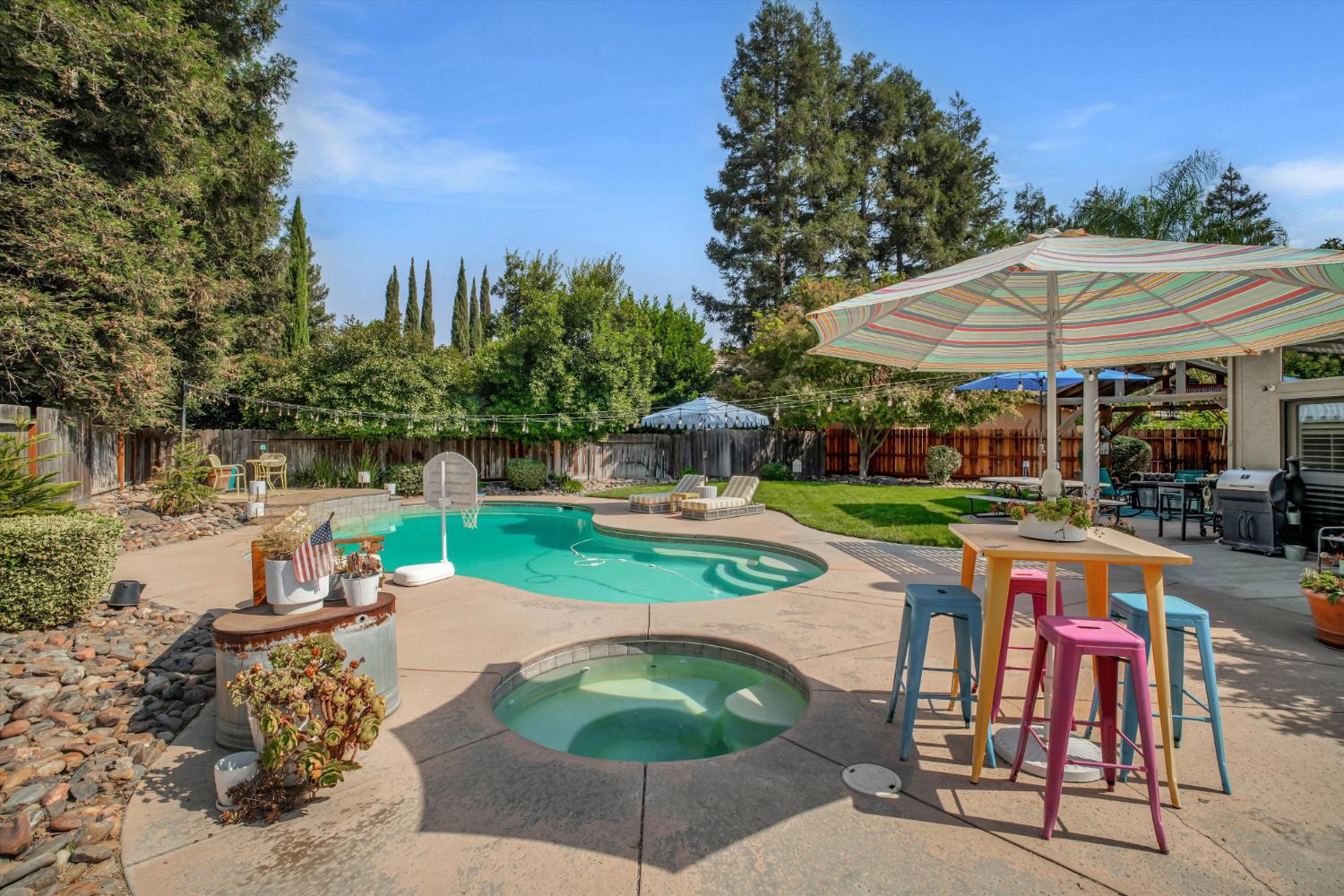 Backyard swimming pool and circular spa beside a striped umbrella and colorful patio stools.