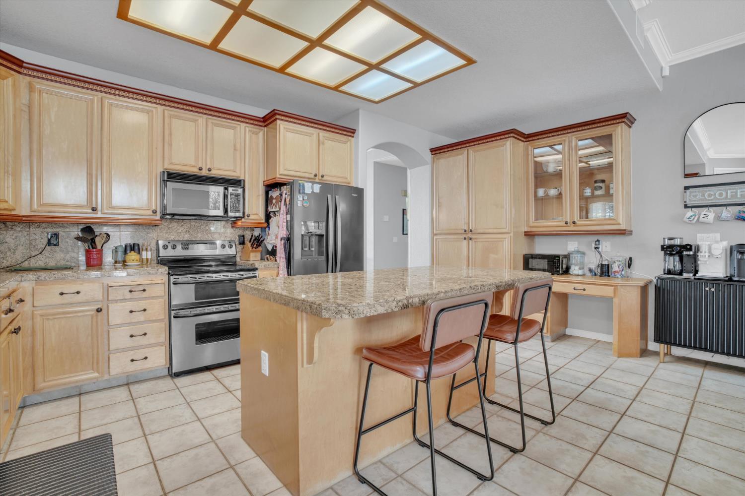 Kitchen with a large granite island, light wood cabinets, and stainless steel appliances.