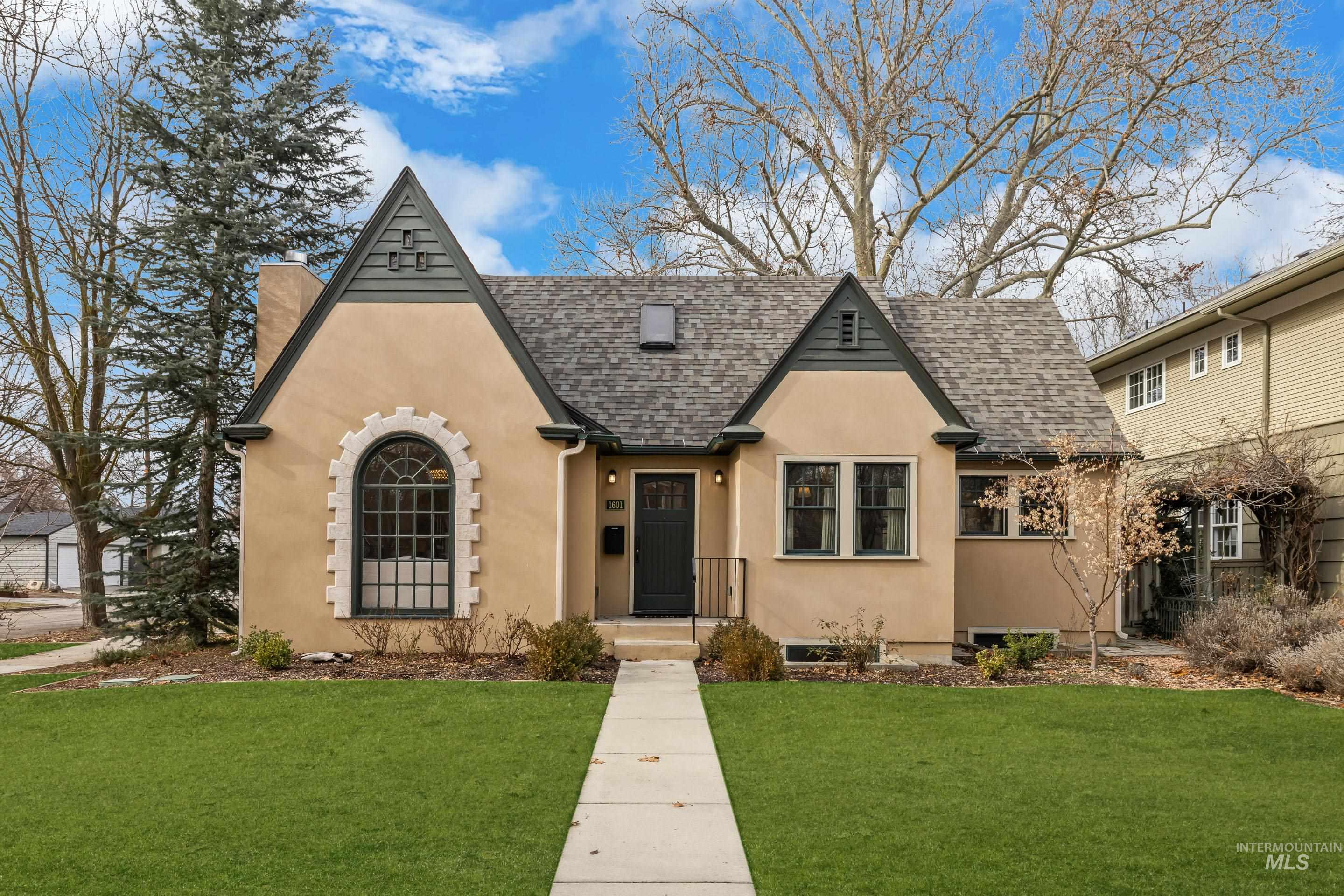 Tan stucco home with steep gables, an arched front window, and a walkway through the lawn.
