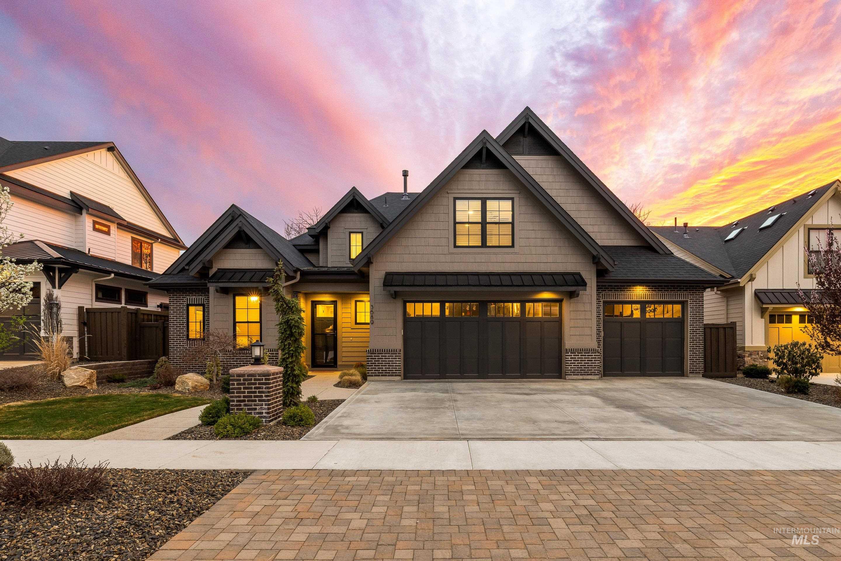 Gray gabled house with brick accents and attached garages beneath a colorful dusk sky.