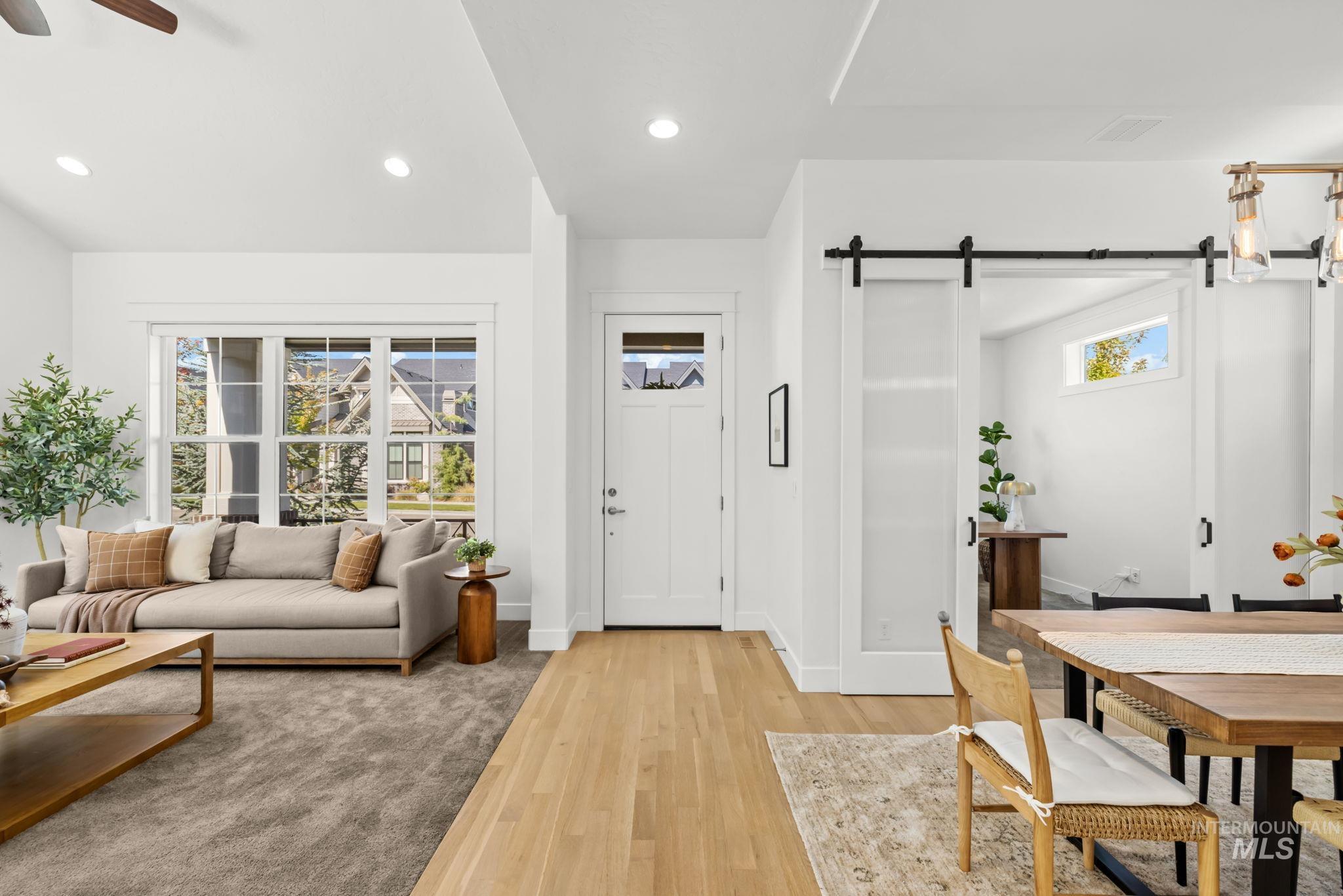 Open-plan living and dining room with a beige sofa, wood floors, and sliding barn door.