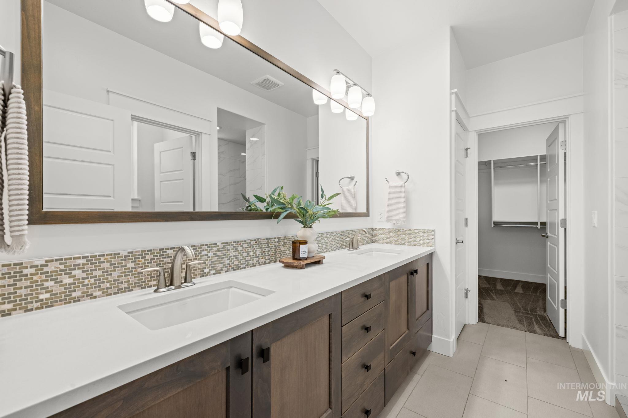 Bathroom with double-sink vanity, mosaic backsplash, and an open doorway to a walk-in closet.