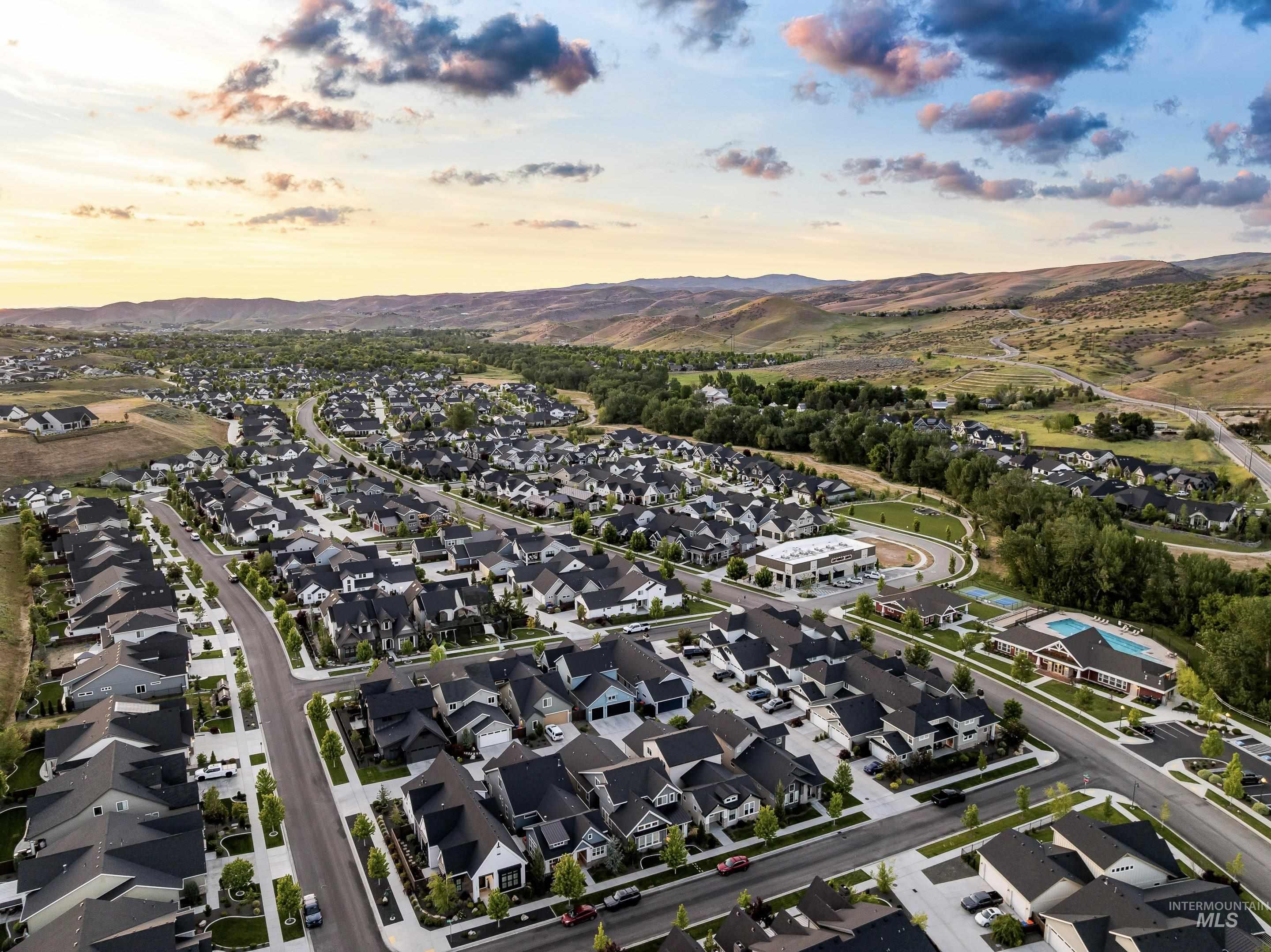 Aerial view of a residential neighborhood and community pool, with foothills beneath a colorful evening sky.