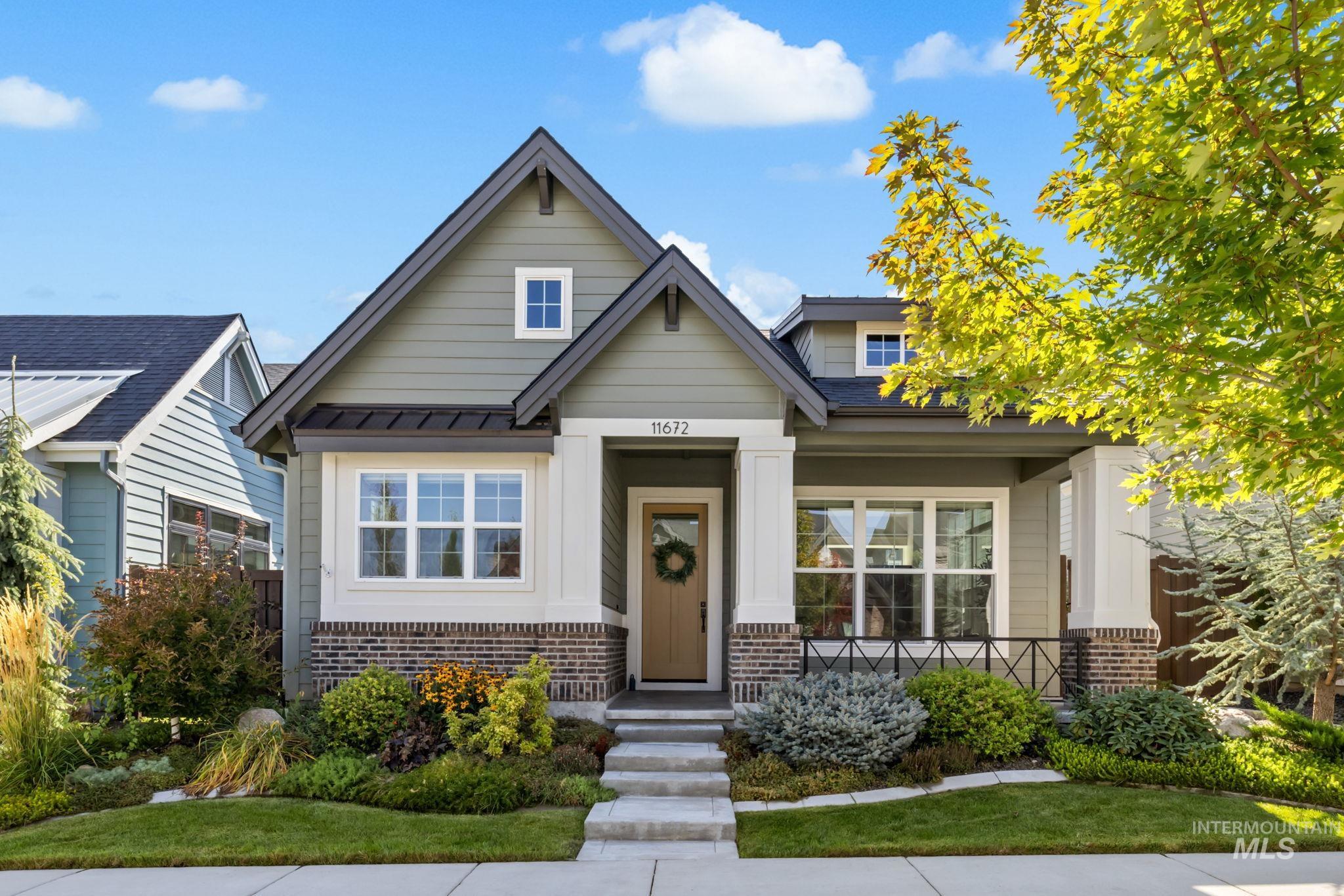Gray-green gabled house with white trim, landscaped garden beds, and yellow autumn leaves.
