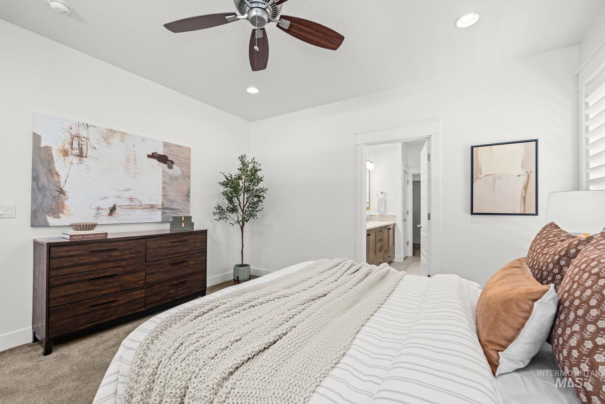 Bedroom with a white striped bed, chunky knit blanket, dark wood dresser, and doorway to an ensuite bathroom.