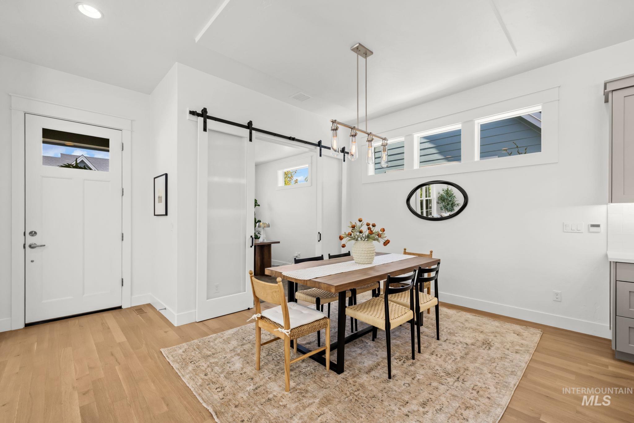 Dining area with a wooden table, mixed chairs, light wood floors, and a black sliding barn door.
