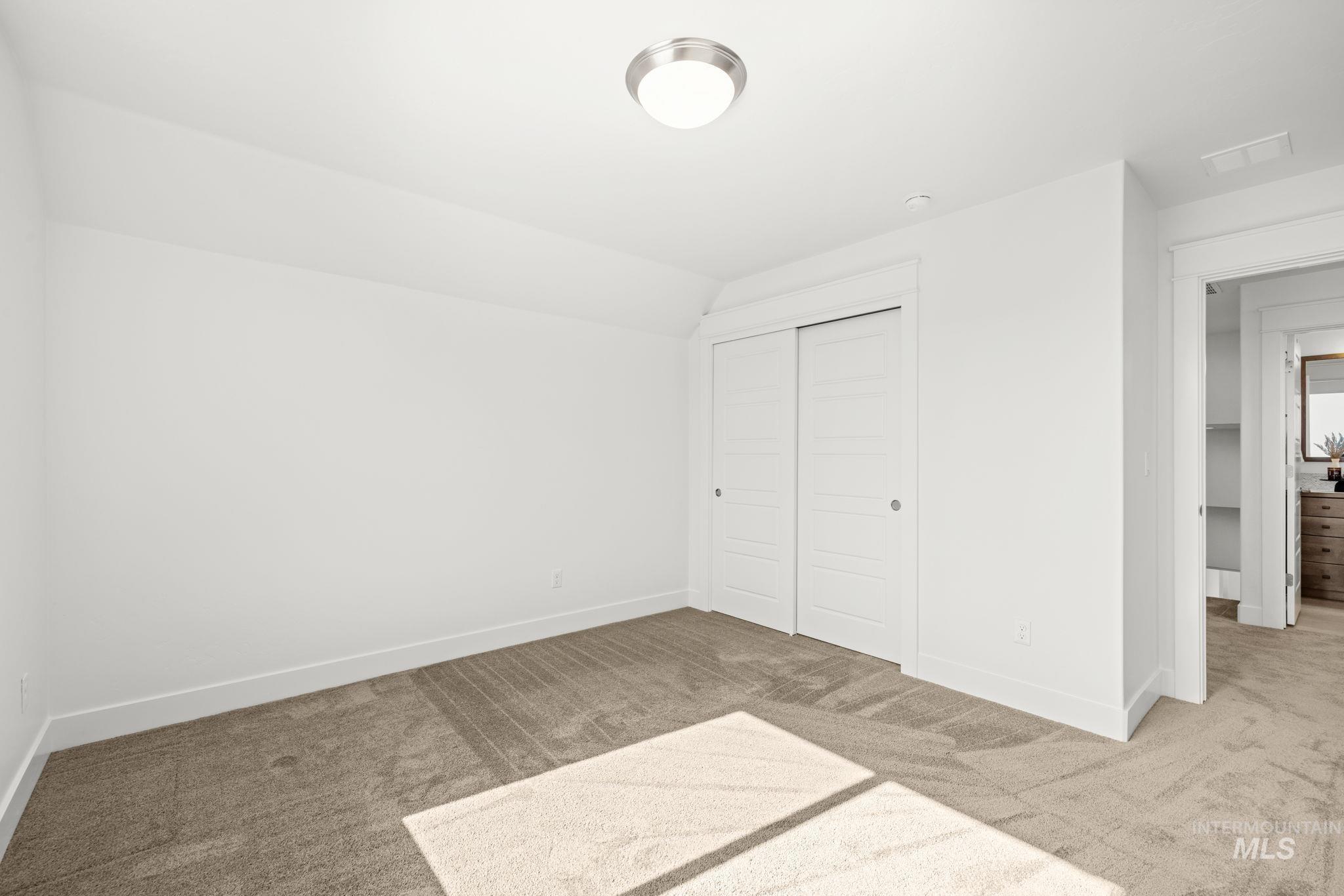Empty carpeted bedroom with a double-door closet and sunlight across the floor.