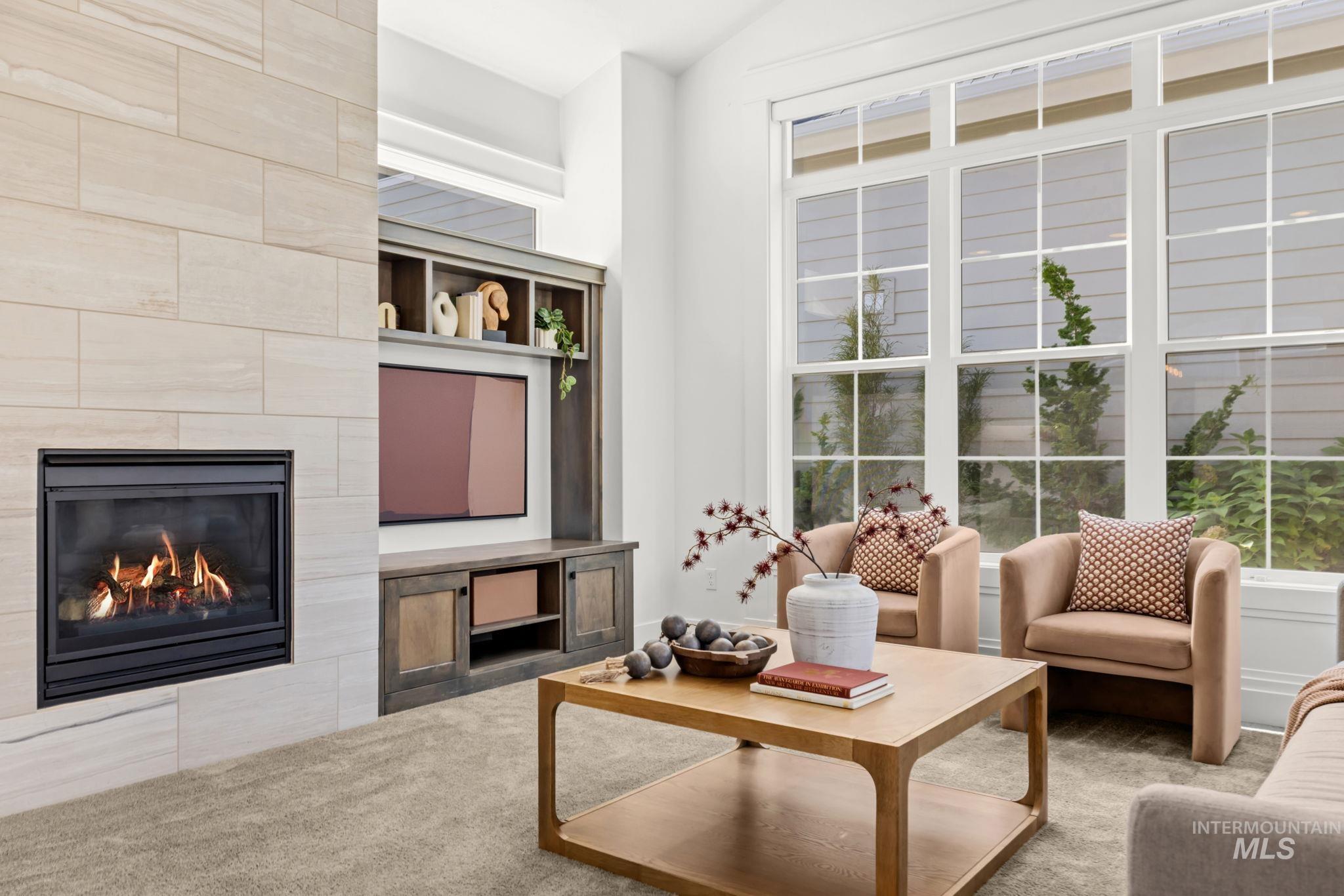 Living room with a stone fireplace, built-in media shelves, and tall windows beside two armchairs.