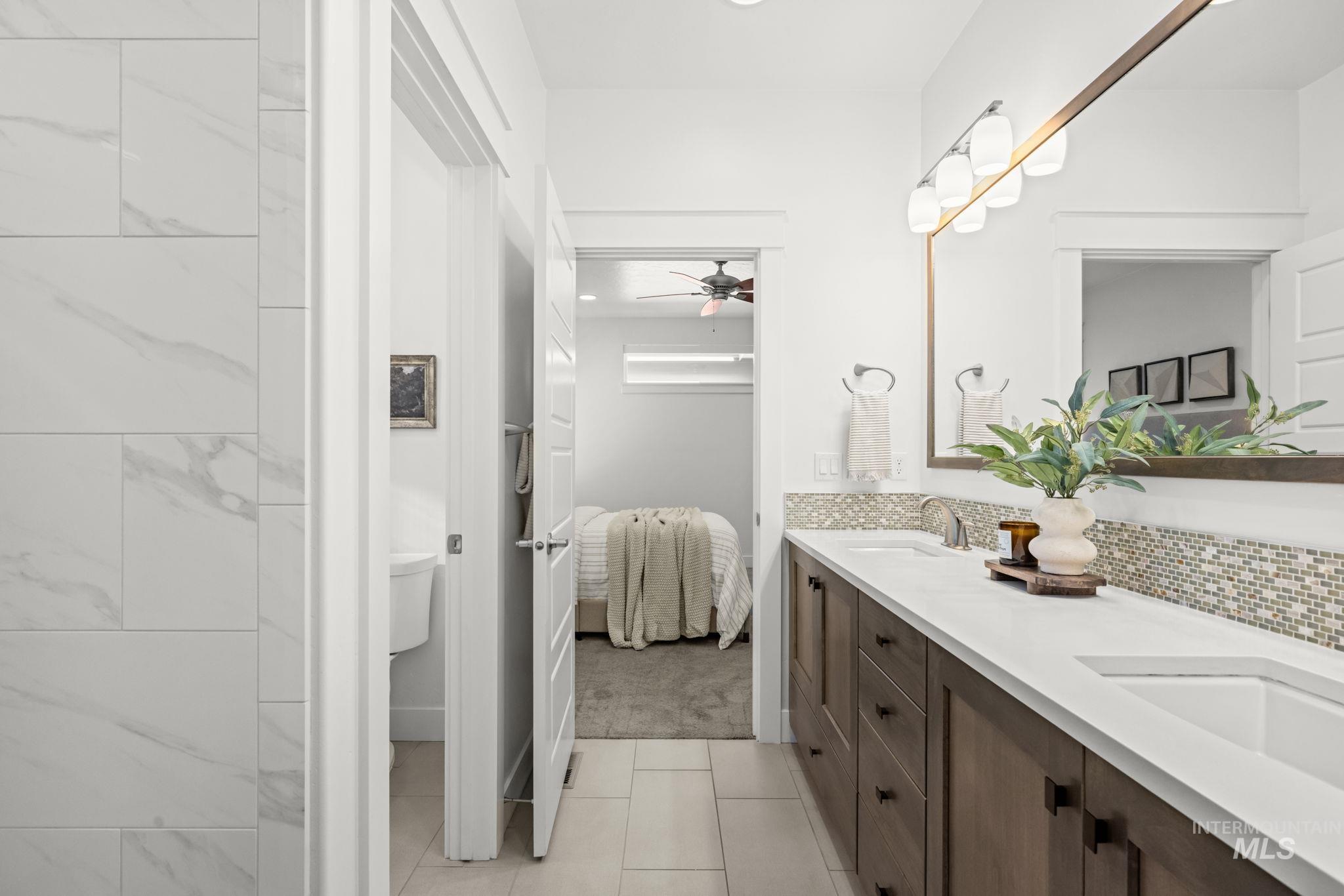 Bright bathroom with a long double vanity and mosaic backsplash, looking through to a bedroom.
