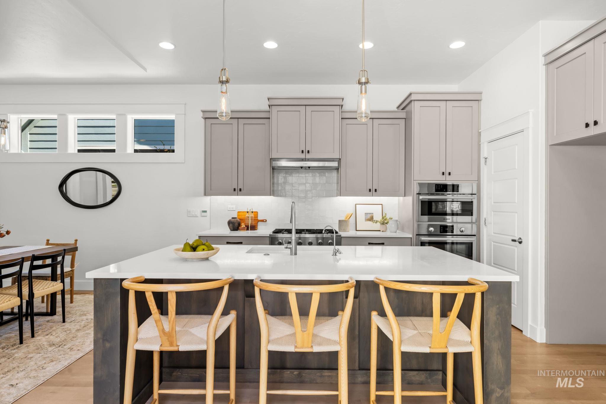 Kitchen with a large white island, three wooden stools, gray cabinets, and stainless steel appliances.