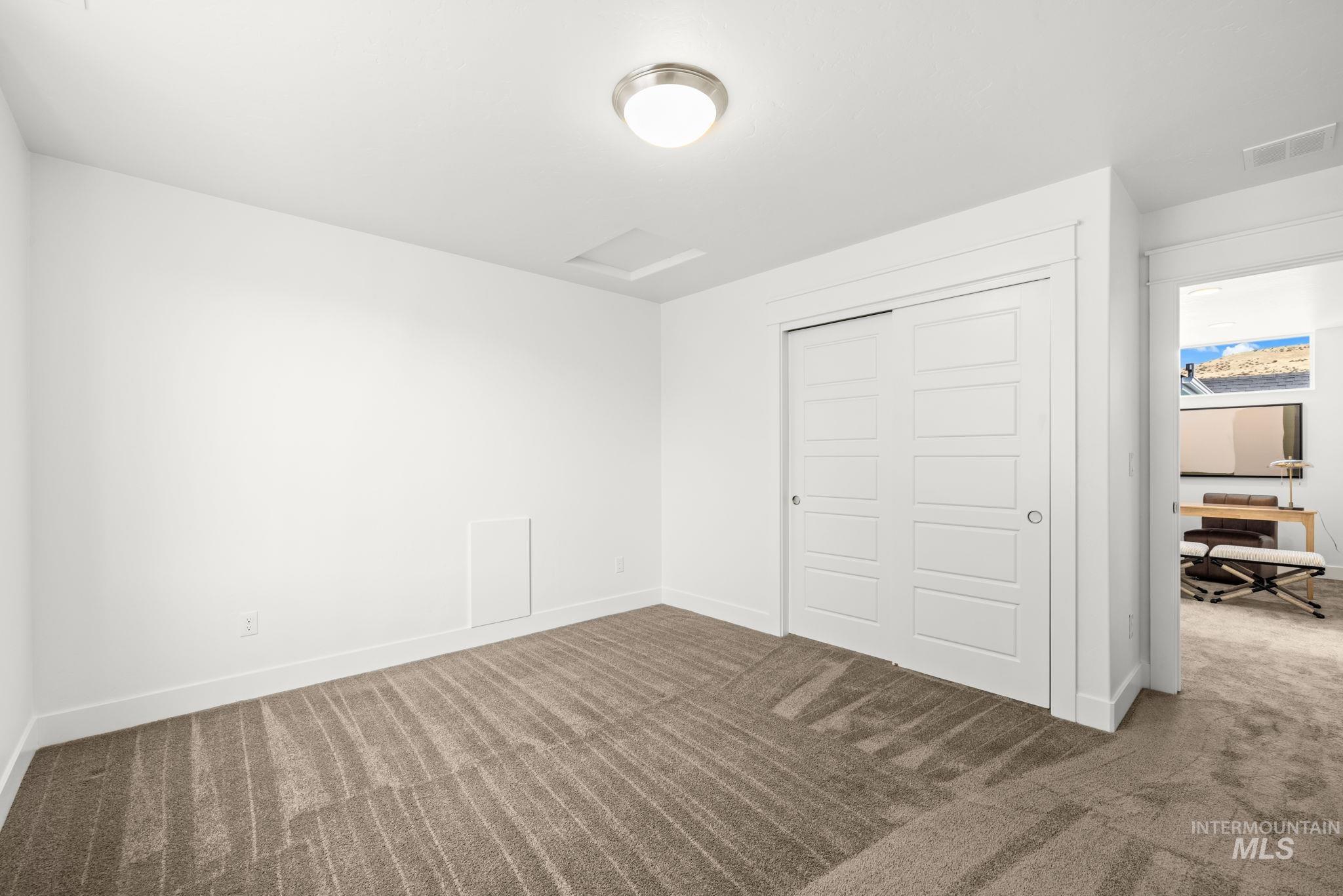 Empty carpeted bedroom with white sliding closet doors and a view into an adjoining furnished room.