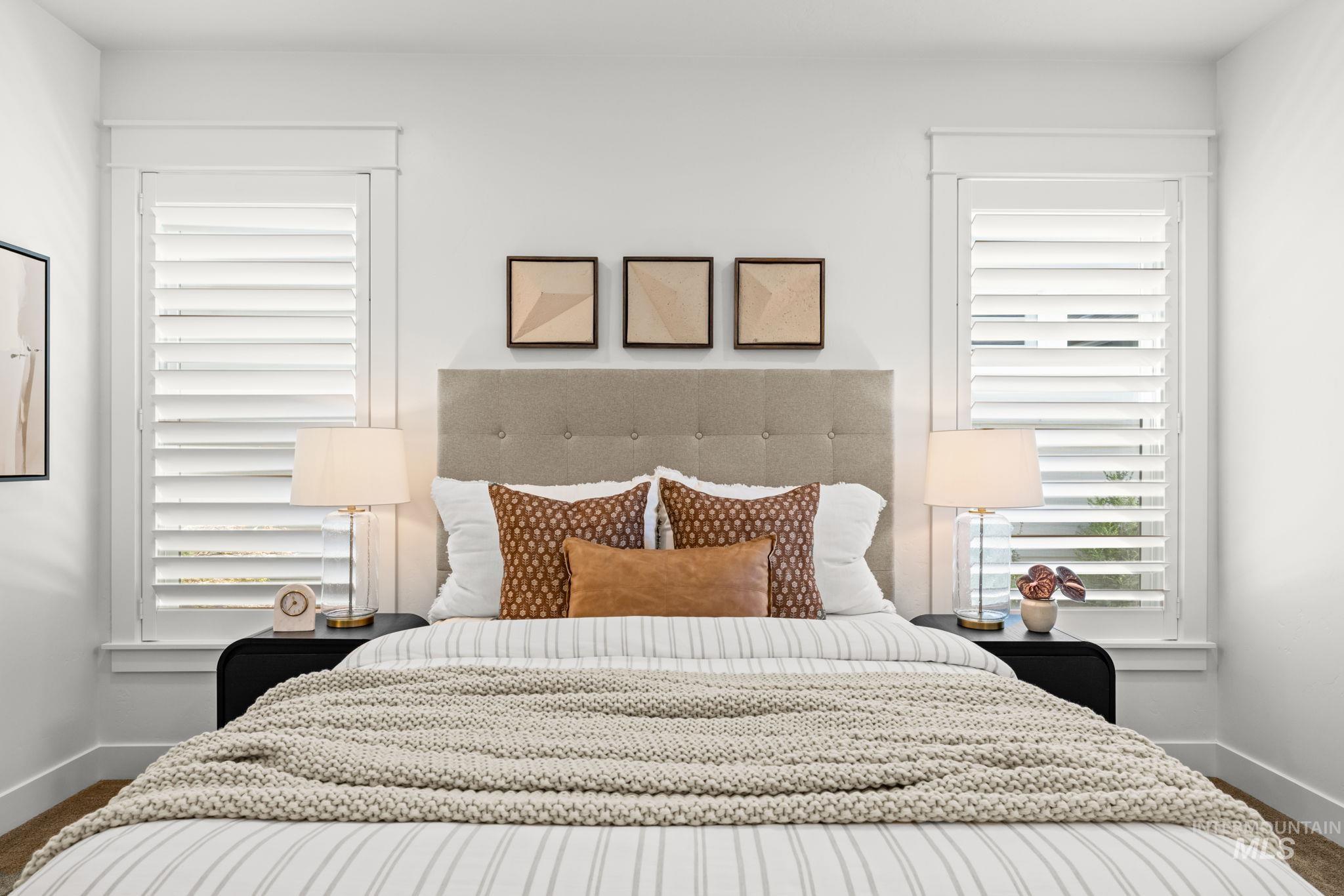 Staged bedroom with a tufted headboard, striped bedding, knit throw, and shuttered windows.