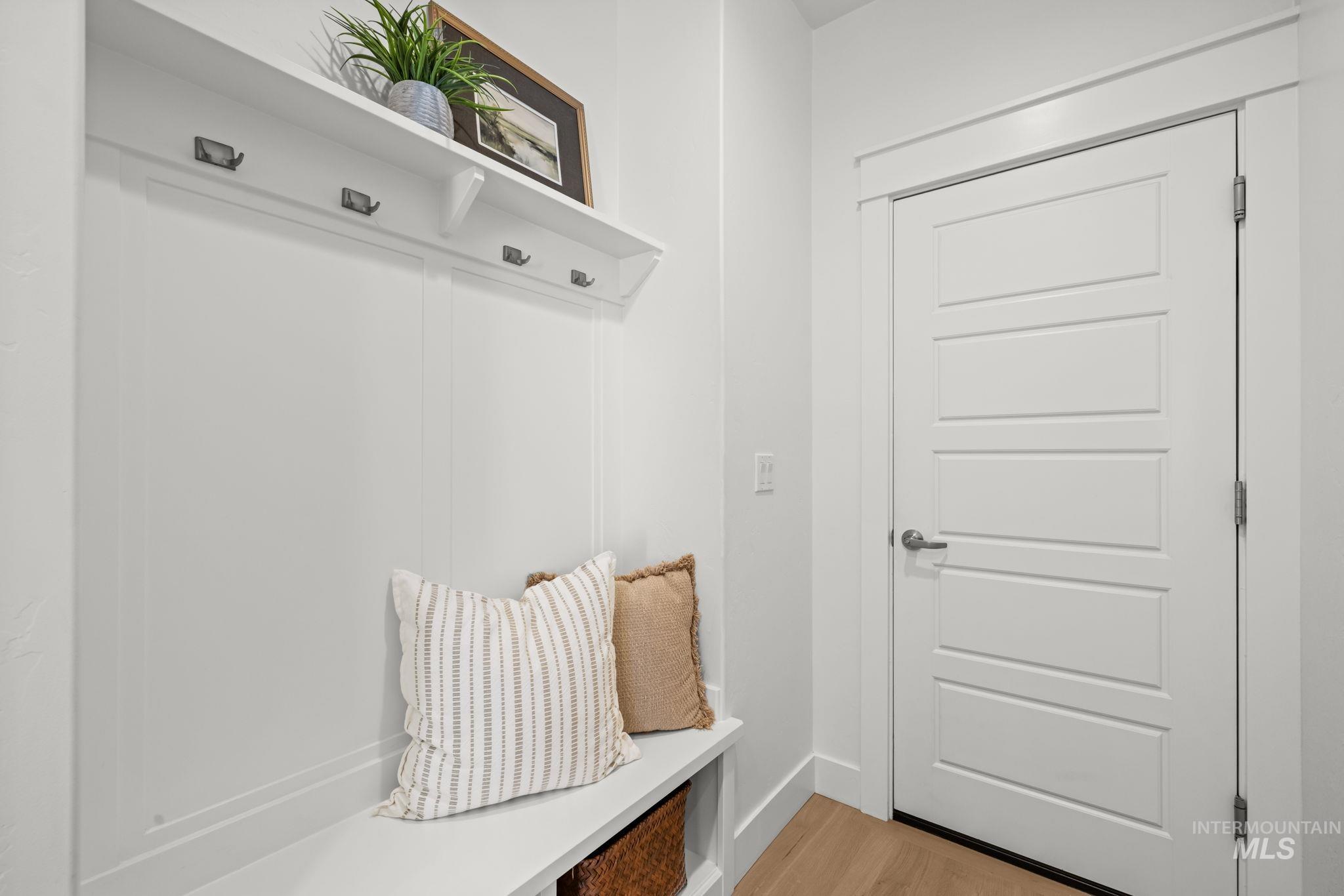 Mudroom entry with a white paneled door, built-in bench, pillows, baskets, and coat hooks.